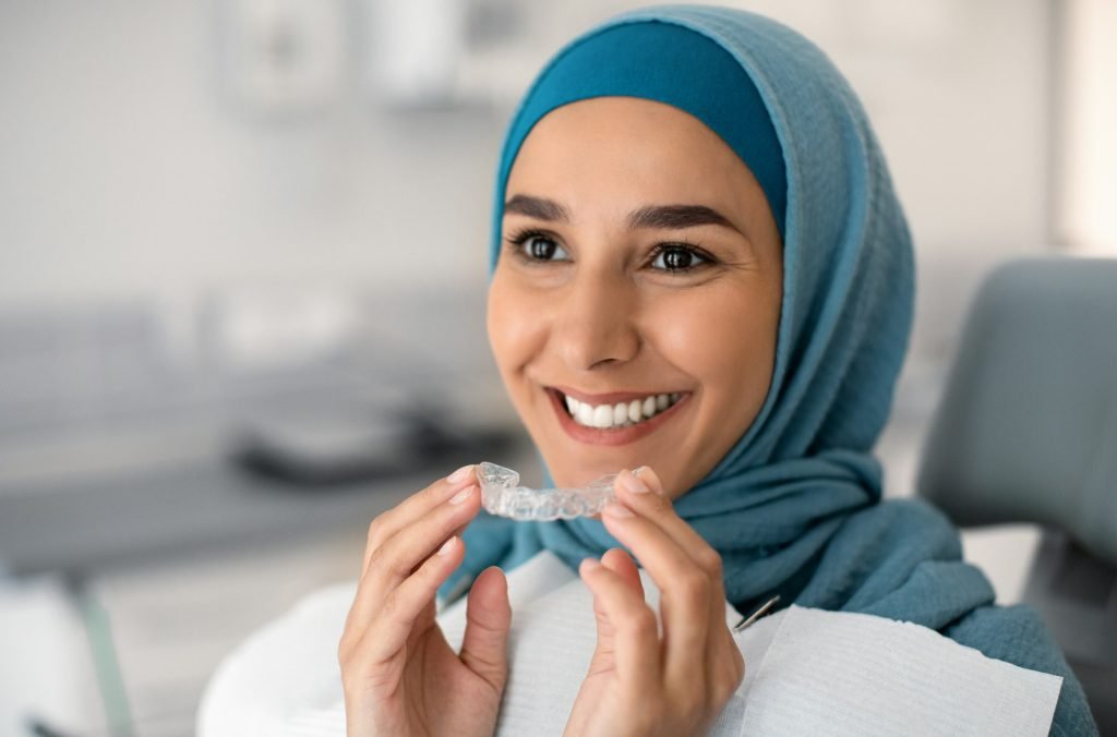 Orthodontics Concept. Smiling Muslim Woman In Hijab Holding Invisalign Or Invisible Braces